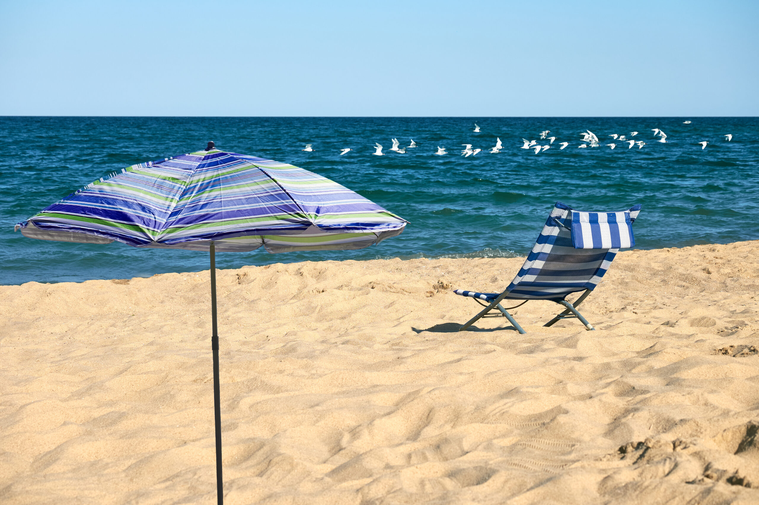 Empty chair and parasol on a quiet beach facing the sea, symbolising calm and peace for travellers with anxiety or depression