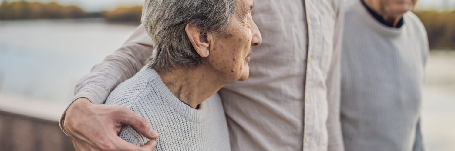 An elderly couple walking in a park with their adult son, symbolising family unity and end-of-life decisions