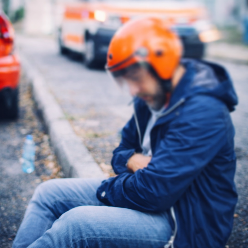 Disoriented man sitting on roadside after accident abroad, wearing a helmet and navy jacket